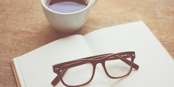 A notebook, glasses and a cup of coffee